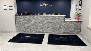 Ein Empfangsbereich mit einer dunkelblauen Wand, einer Arbeitsplatte im Steinoptik und einem Logo mit der Aufschrift "Baymont by Wyndham".