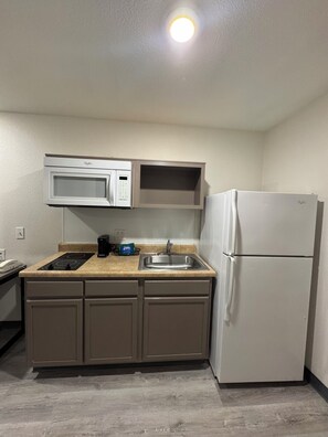 A compact kitchen with a microwave, stove, sink, and refrigerator. - Baymont by Wyndham Dickinson (Dickinson)