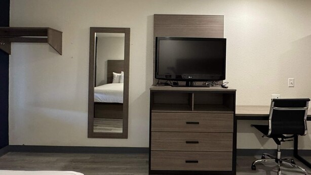 Ein Hotelzimmer mit Bett, Fernseher auf einem Holztisch, Schreibtisch mit Stuhl und Spiegel an der Wand.