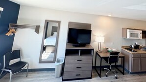 A compact hotel room with a bed, a desk with a chair, a television, a microwave, a refrigerator, and a small kitchenette. - Baymont by Wyndham Dickinson (Dickinson)