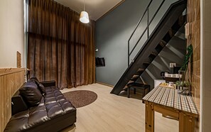 A modern living room with a leather sofa, a wooden dining table, and a staircase. - Hotel Hue Loft (Incheon)
