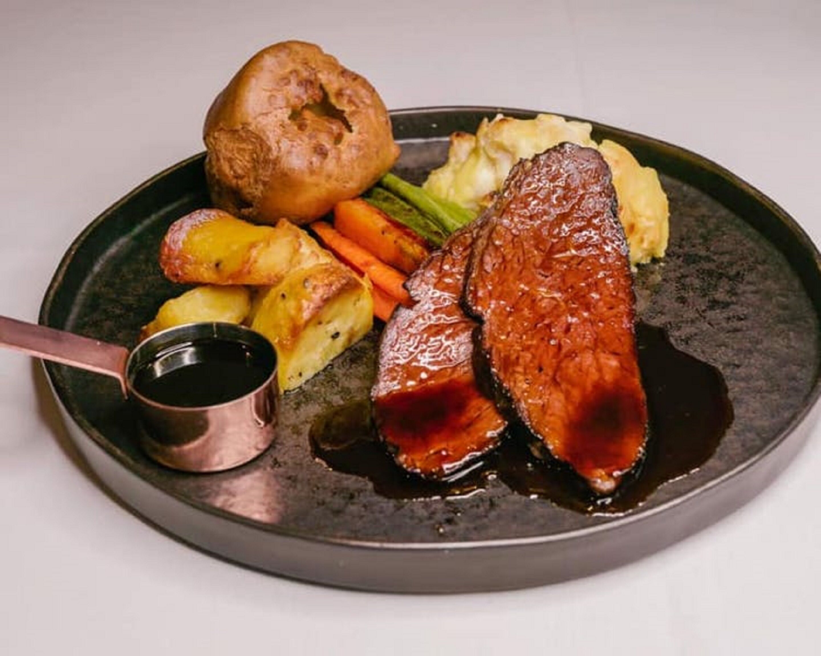A plate with steak, roasted potatoes, carrots, and a Yorkshire pudding.