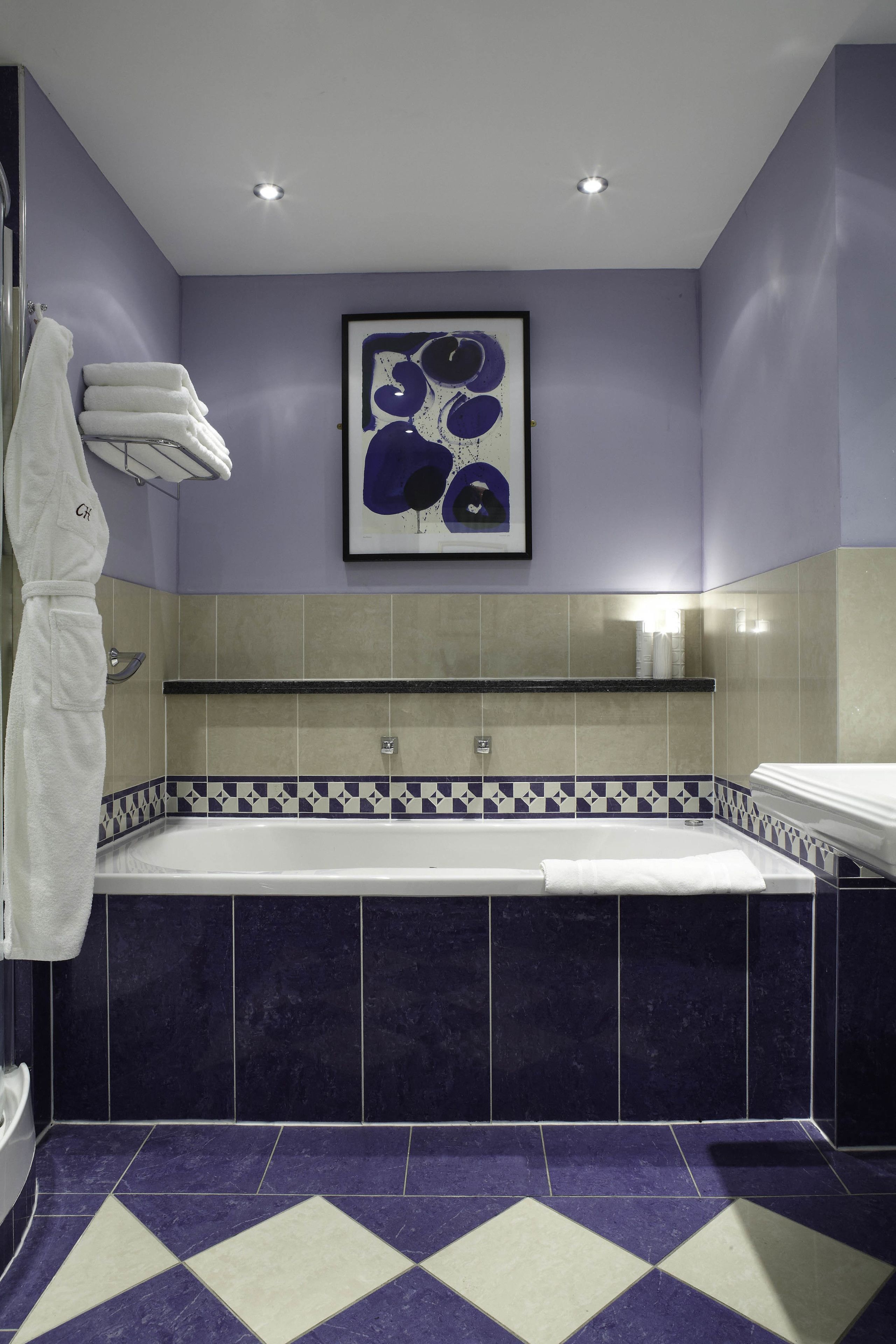 A modern bathroom with a large bathtub, a towel rack with towels, and a framed artwork on the wall.