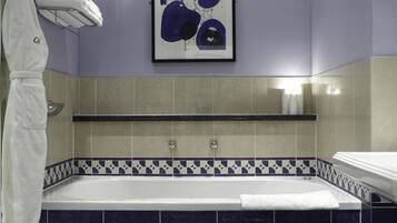A modern bathroom with a large bathtub, a towel rack with towels, and a framed artwork on the wall.