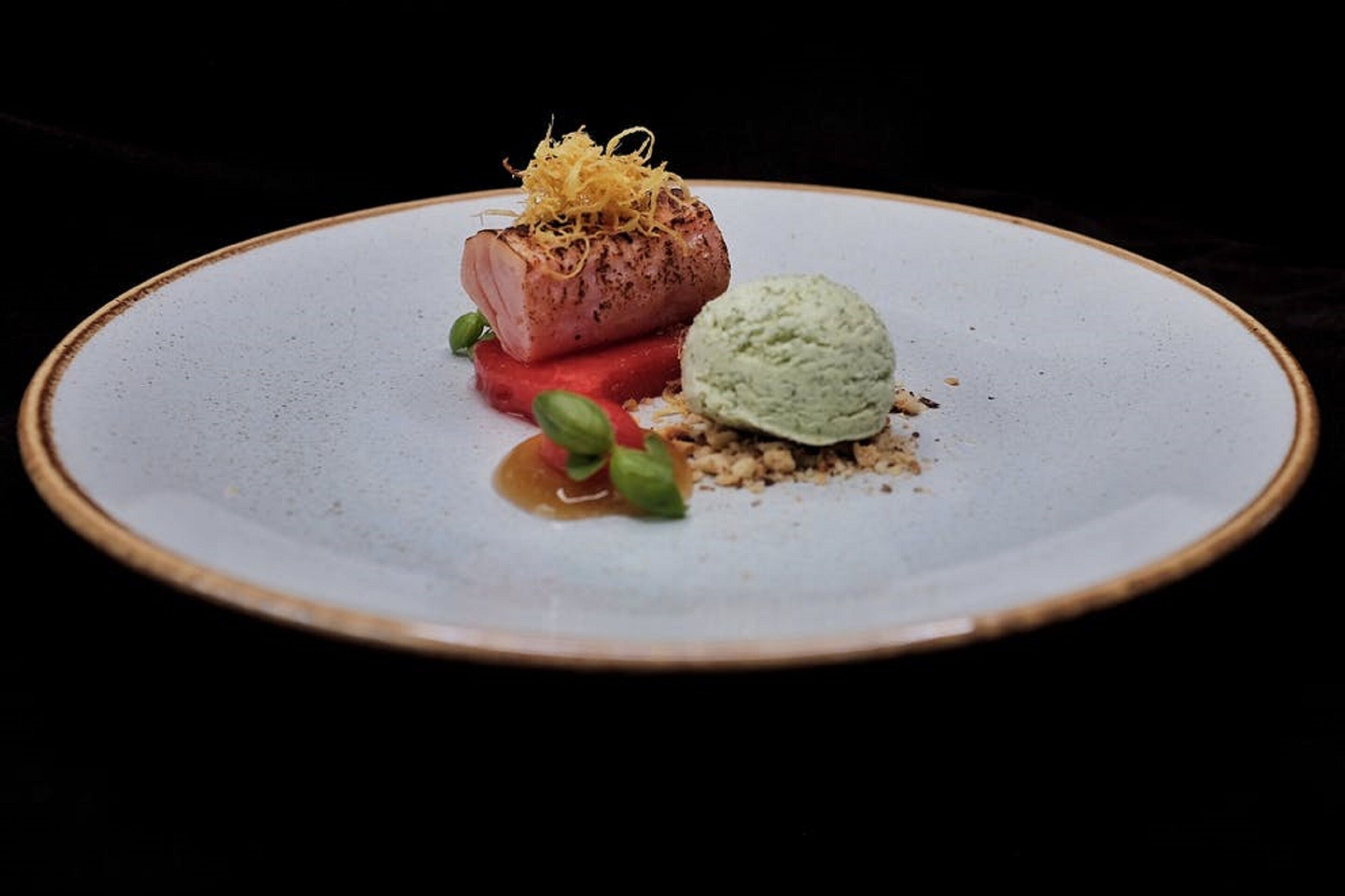 Un plato con un trozo de carne, una porción de helado verde y algunos adornos.