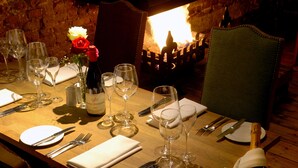 A dining table set with wine glasses, plates, cutlery, and a bottle of champagne, with a brick wall and a fireplace in the background. - Cantley House Hotel (Wokingham)
