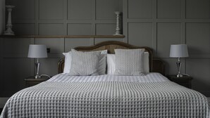 A neatly made bed with a patterned bedspread and pillows, flanked by two bedside tables with lamps, against a paneled wall with a decorative shelf. - Cantley House Hotel (Wokingham)