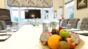 A conference room with a long table, chairs, a fruit bowl, and bottles of water. - Cantley House Hotel (Wokingham)