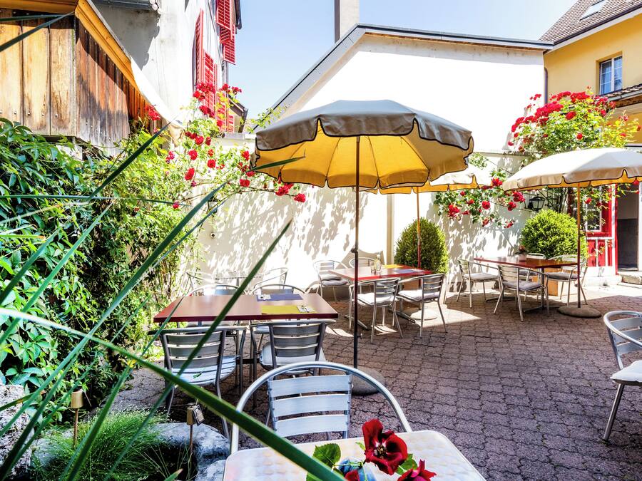 Un patio al aire libre con mesas y sillas, rodeado de follaje y flores.