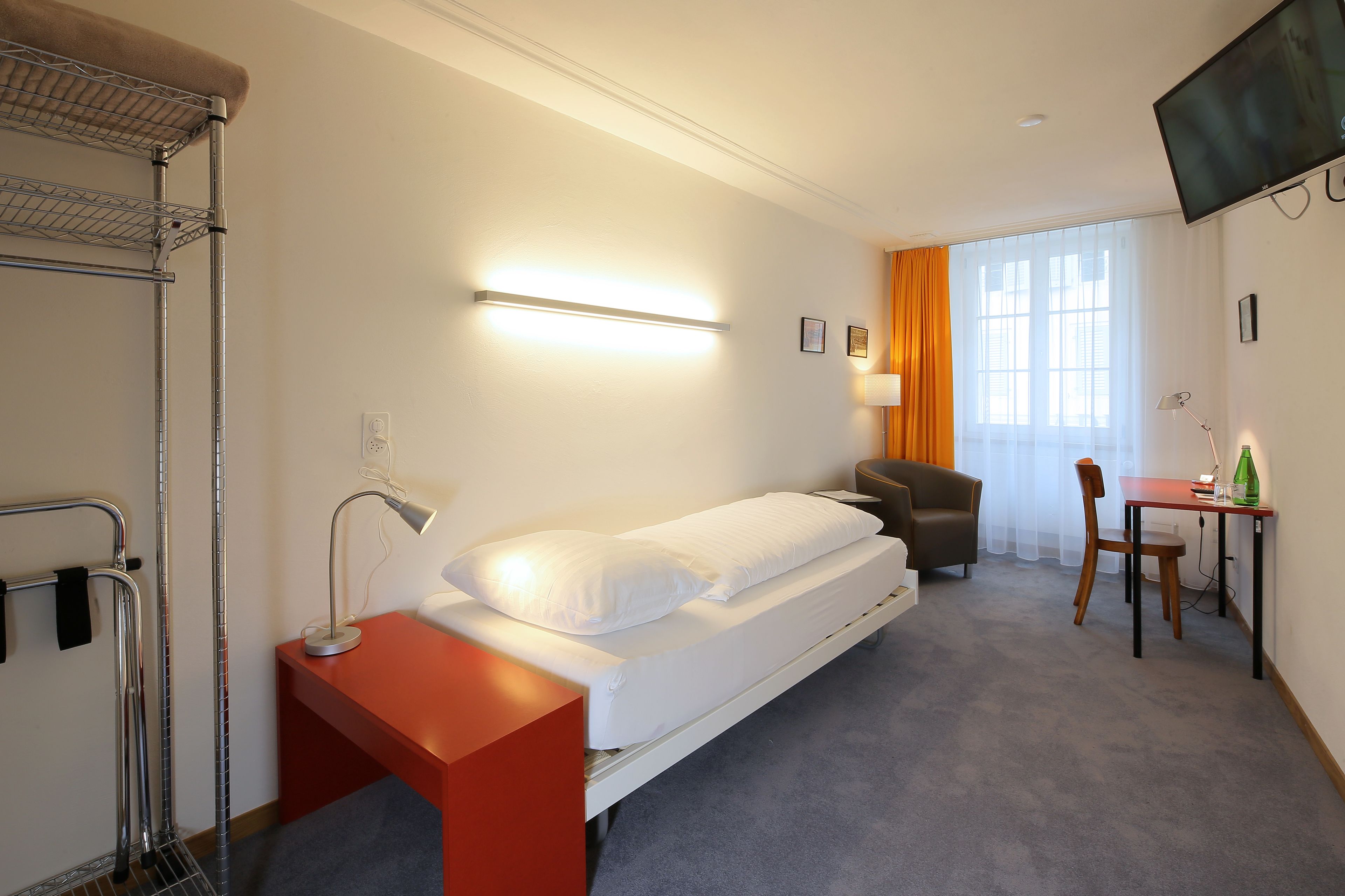 A hotel room with a bed, a desk, a chair, a TV, and a window with curtains.