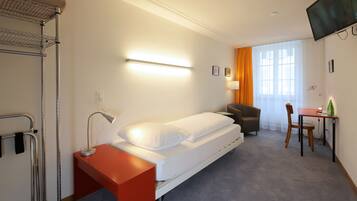 A hotel room with a bed, a desk, a chair, a TV, and a window with curtains.