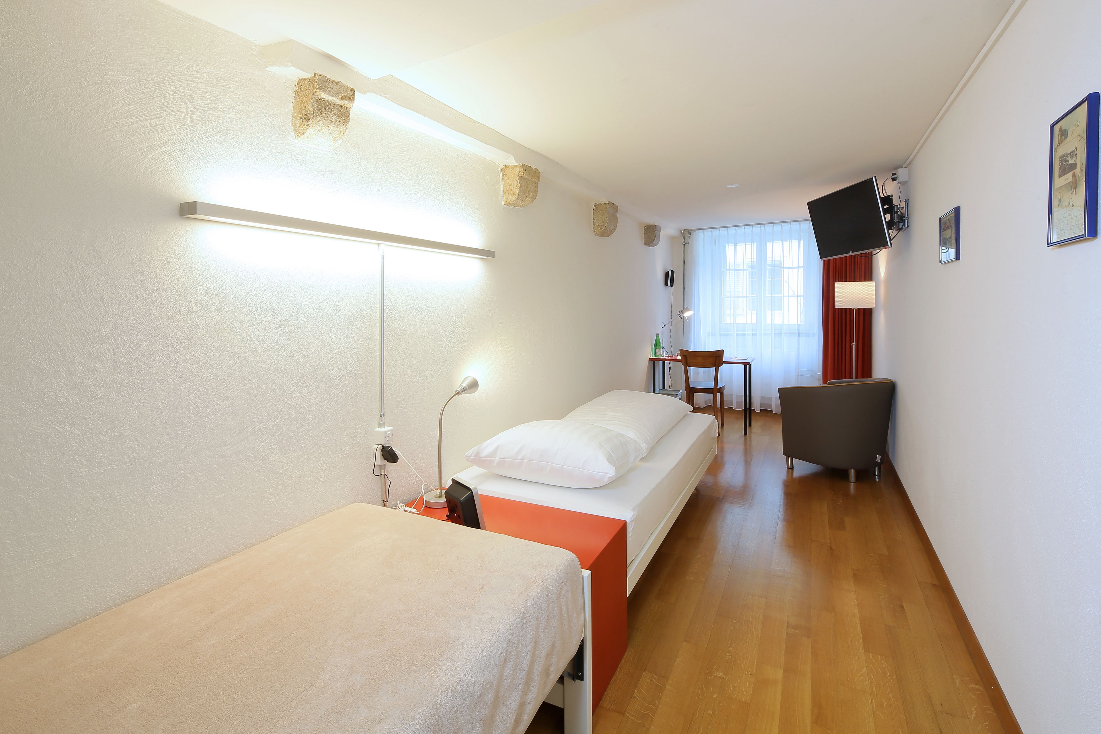 A hotel room with two beds, a desk, a chair, and a TV.