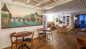 A dining area with wooden tables and chairs, a mural of a castle on the wall, and a view of the outside through a window. - Hotel Roter Ochsen (Solothurn)
