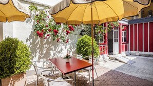 An outdoor patio with a table and chairs, a yellow umbrella, and red flowers against a white wall. - Hotel Roter Ochsen (Solothurn)