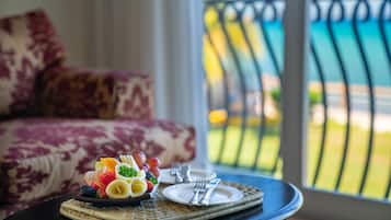 A dining table with a fruit platter and cutlery, a sofa with a patterned cushion, and a view of a balcony with a railing.