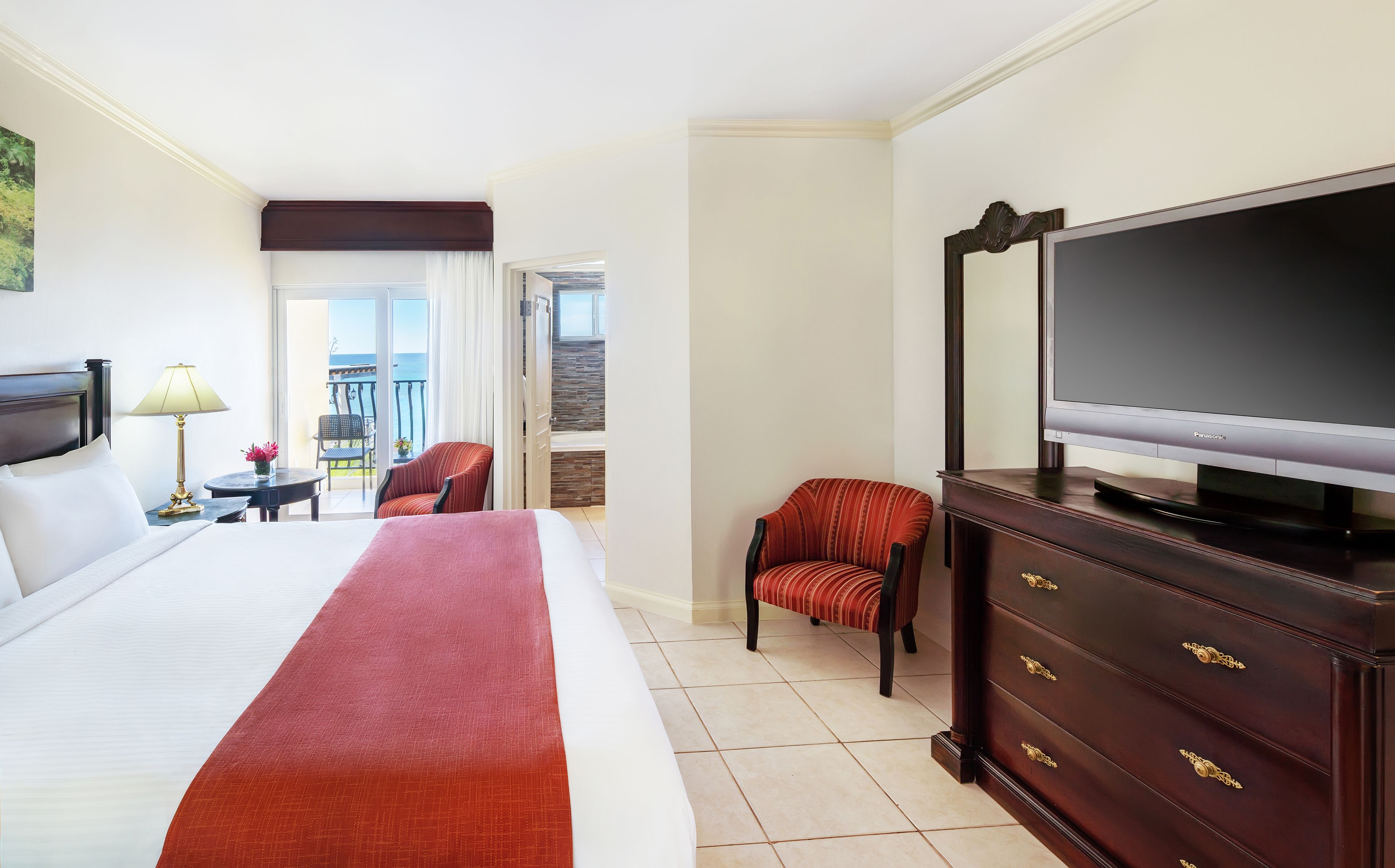 A hotel room with a large bed, a television, a dresser, and a chair.