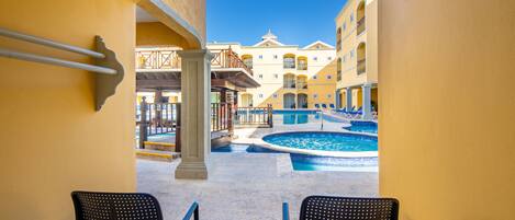 A view through an archway of a pool area with two chairs and a table, a pool, and buildings in the background.