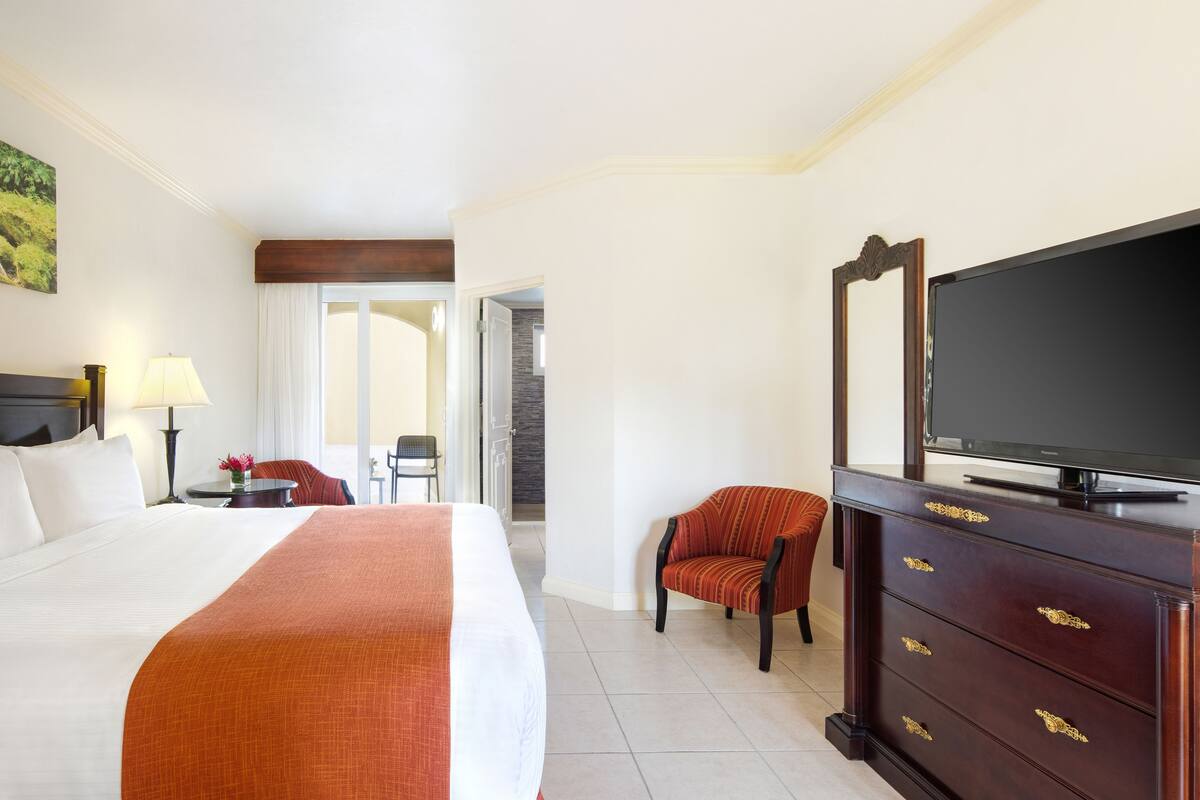 Une chambre d’hôtel avec un grand lit, un téléviseur posé sur une commode et un fauteuil.