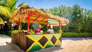 Un stand de restauration situé en bord de mer, appelé « Seaside Jerk Hut », avec un toit de chaume et une structure en bois aux couleurs vives.