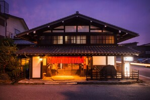 A traditional Japanese building with a tiled roof, wooden structure, and a small entrance area with a lantern and a signboard.