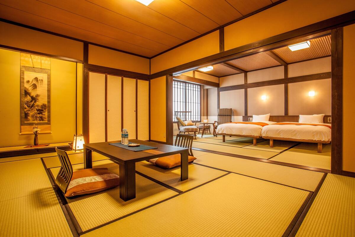 Une pièce de style japonais traditionnel, avec un sol recouvert de tatamis, une table basse, deux lits et une vue sur l’extérieur.