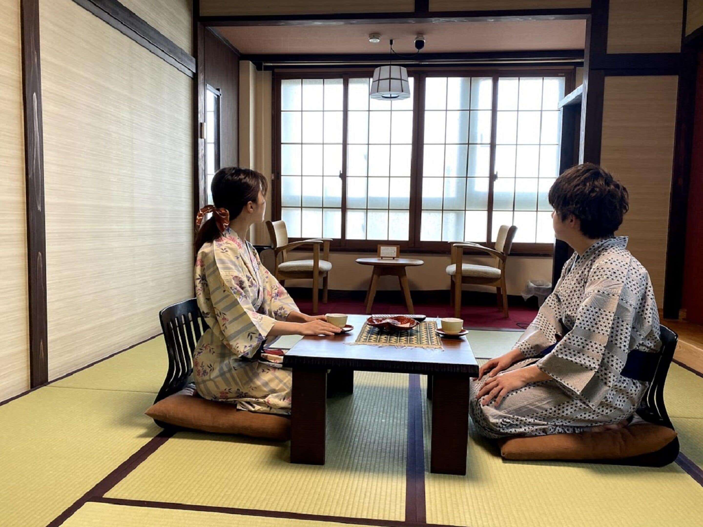 A traditional Japanese room with tatami flooring, a low table, and two people seated facing each other.