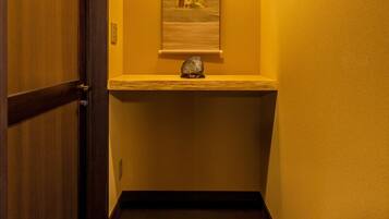 A hallway with a wooden door, a framed picture on the wall, and a small shelf with a decorative item.