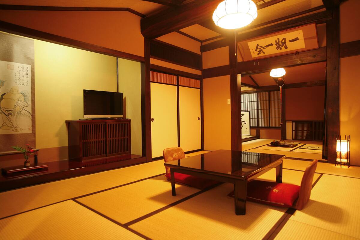 Une pièce de style japonais traditionnel, avec un sol recouvert de tatamis, une table basse et un téléviseur posé sur un meuble.
