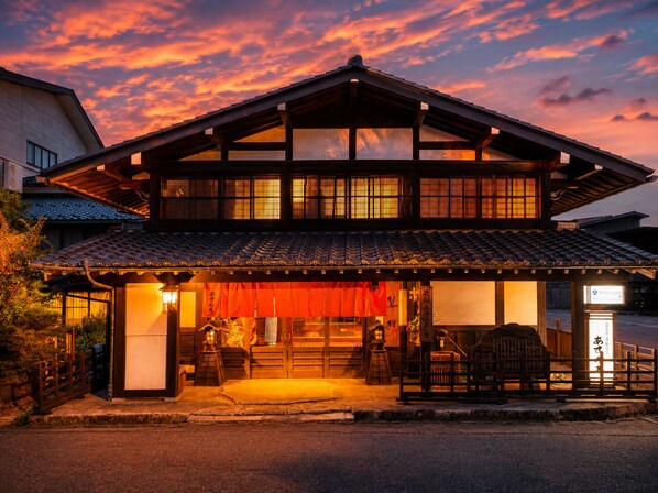 A traditional Japanese building with a tiled roof and wooden structure, featuring a covered entrance and a signboard.