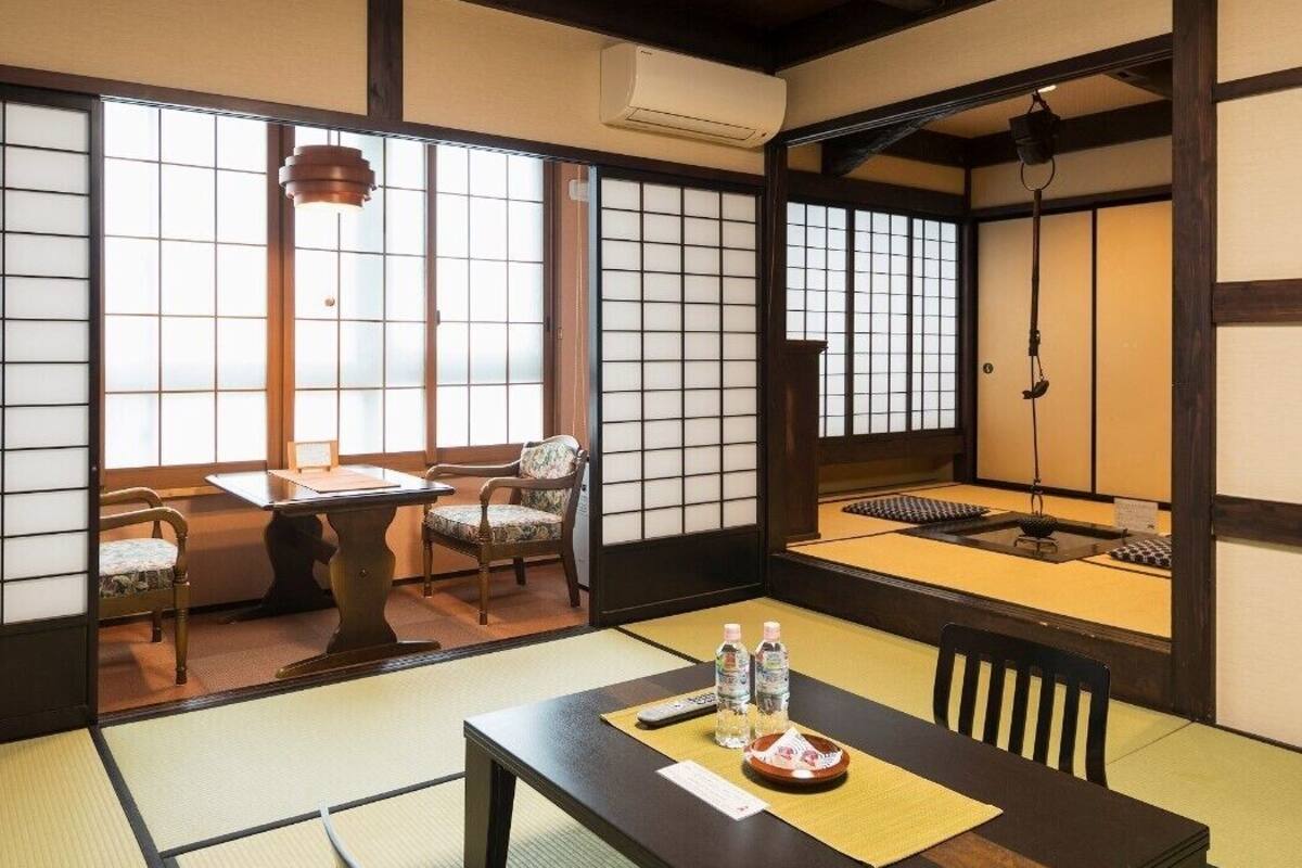 Una habitación japonesa tradicional con suelo de tatami, una mesa baja con cojines, un farol colgante y puertas correderas.