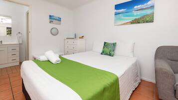 Une chambre d’hôtel avec un lit, une chaise, un bureau et une salle de bain, visibles à travers une porte ouverte.