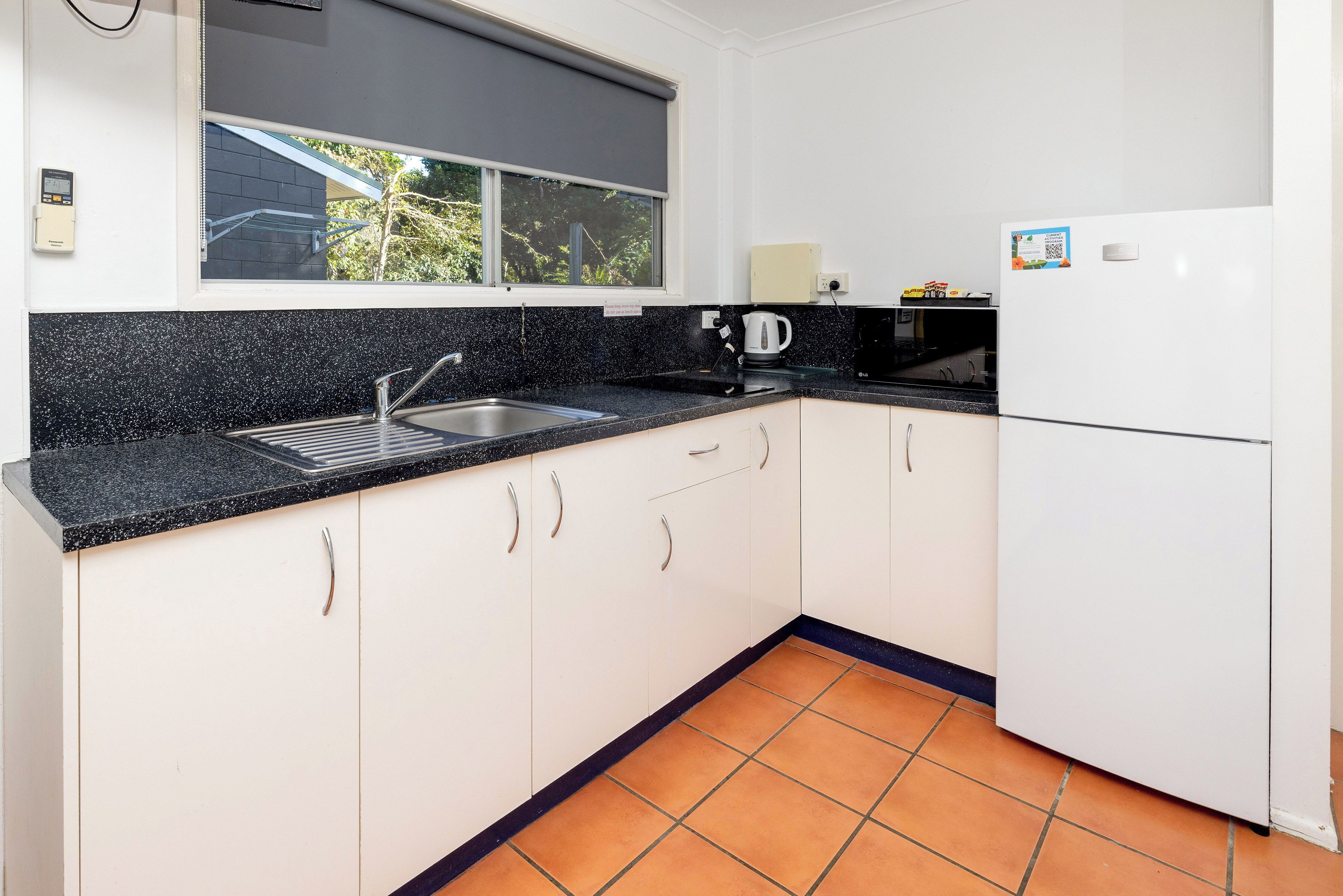 Una cocina compacta con un lavamanos, un hervidor y un refrigerador blanco.