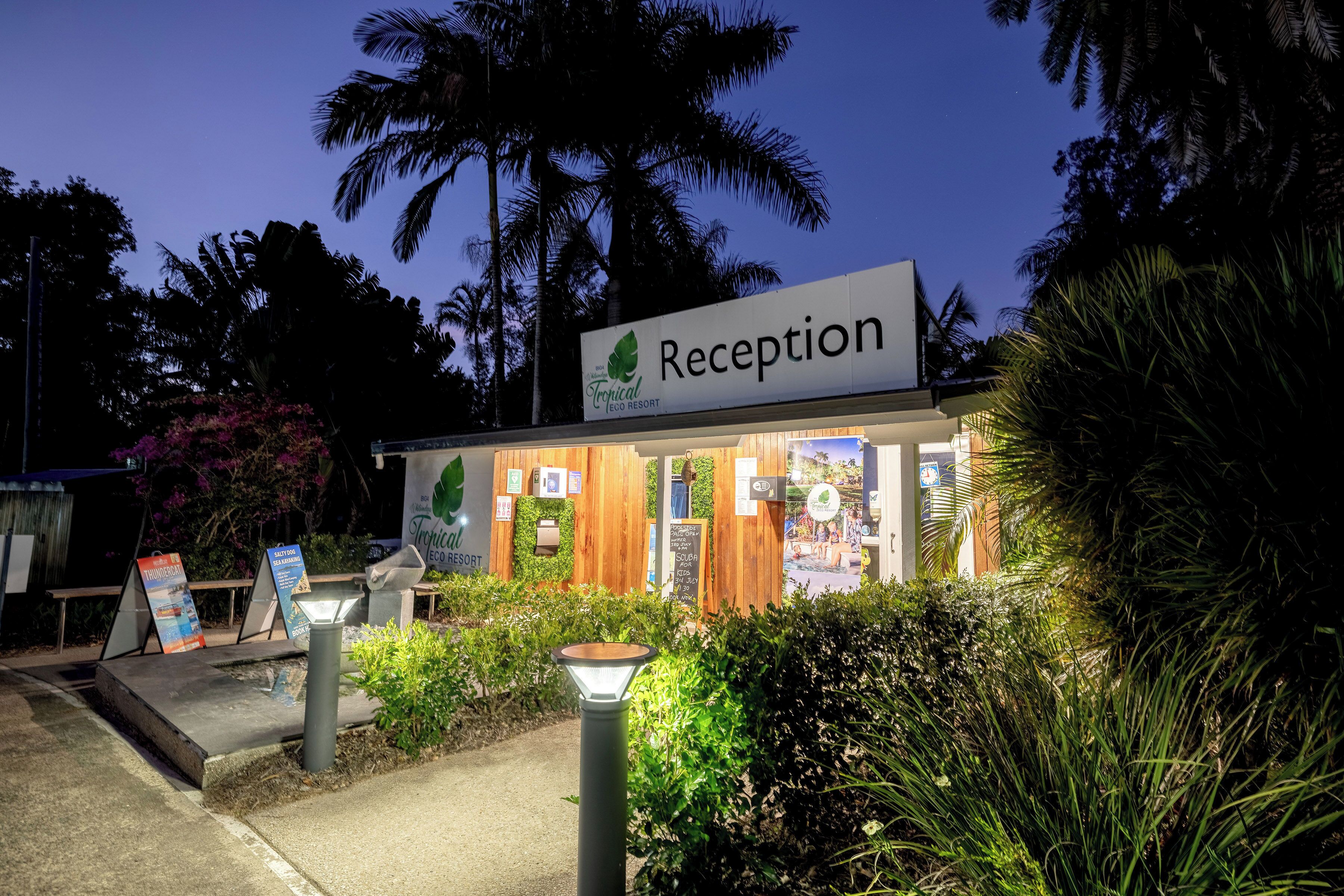 Een receptiegedeelte bij Tropical Eco Resort, met een bord, houten gevel en beplanting.