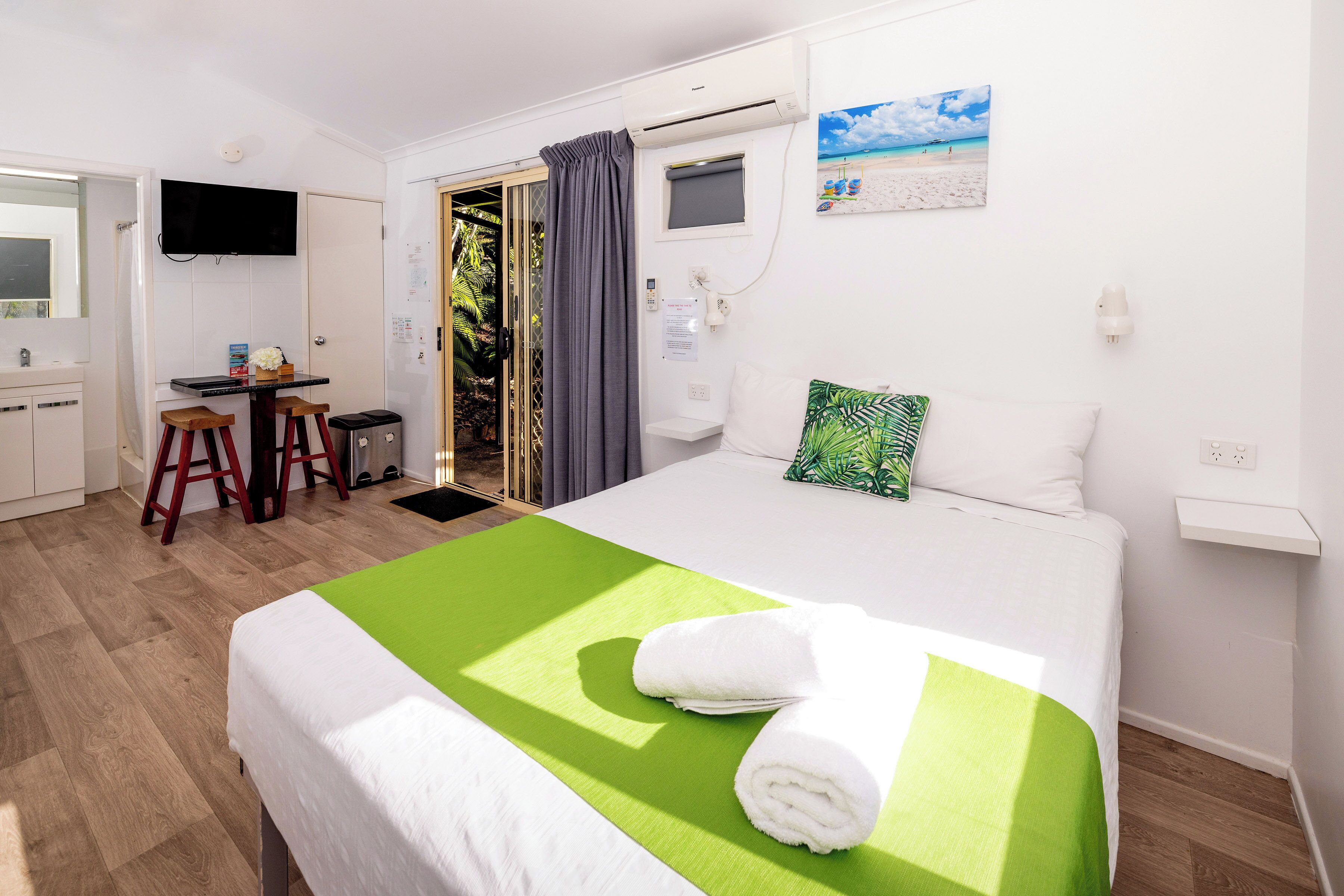 A hotel room with a bed, a desk, and a shower area.