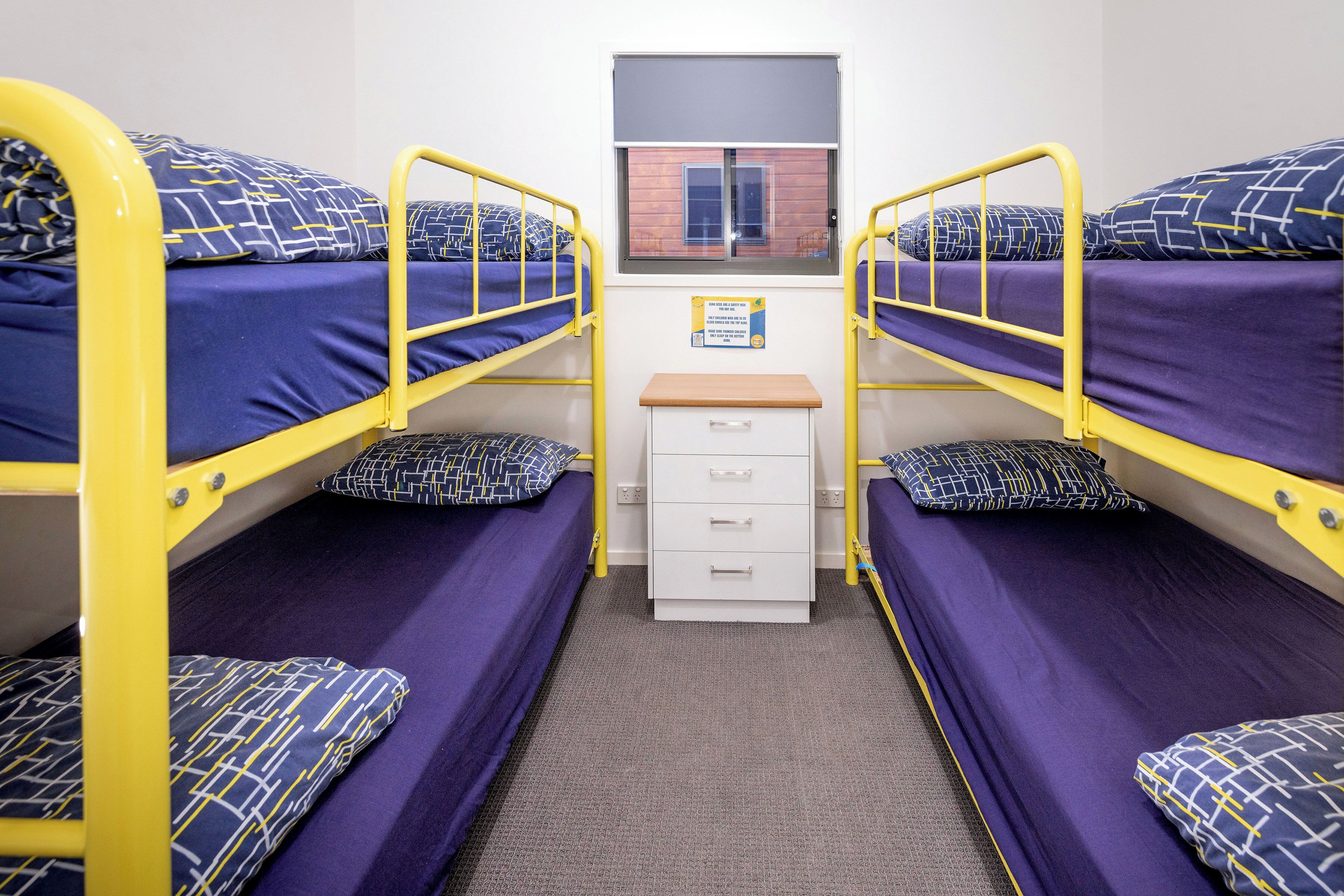A dormitory room with bunk beds, a small desk, and a window.