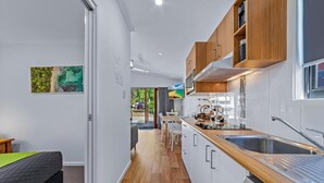A modern kitchen with wooden cabinets, a stainless steel sink, and a dining area with white chairs. - BIG4 Whitsunday Islands Holiday Park (Flametree)