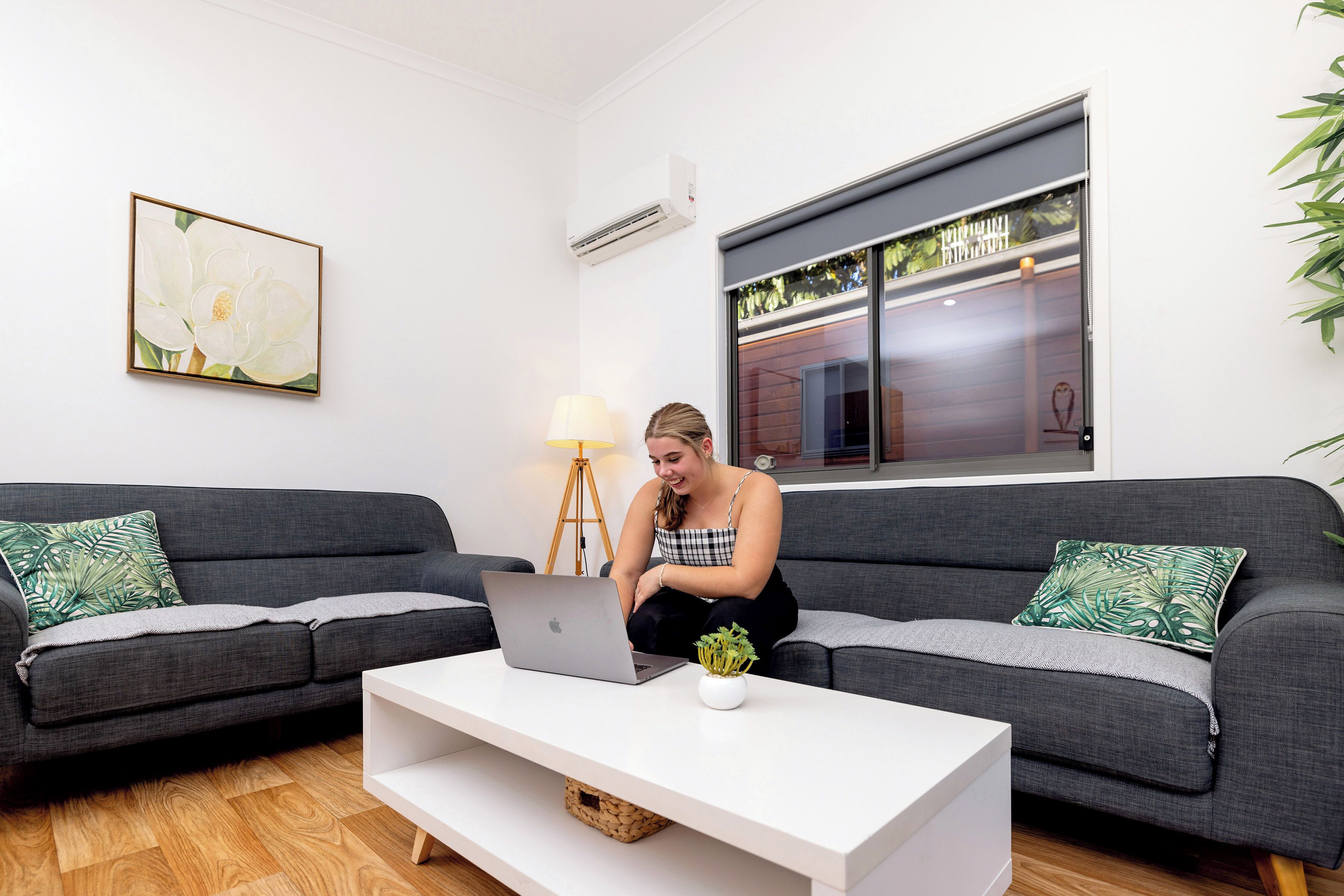 A modern living room with a grey sofa, a white coffee table, and a laptop.