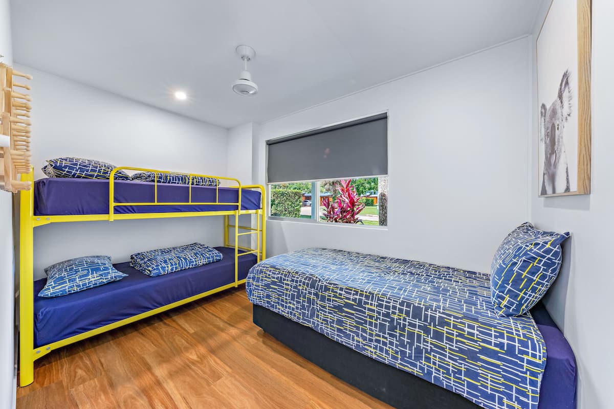 Une chambre avec un lit superposé, un lit simple, une fenêtre donnant sur un beau paysage et un luminaire au plafond.