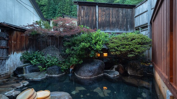 Un jardín japonés tradicional con un estanque de carpas, estructuras de madera y una pequeña cascada.