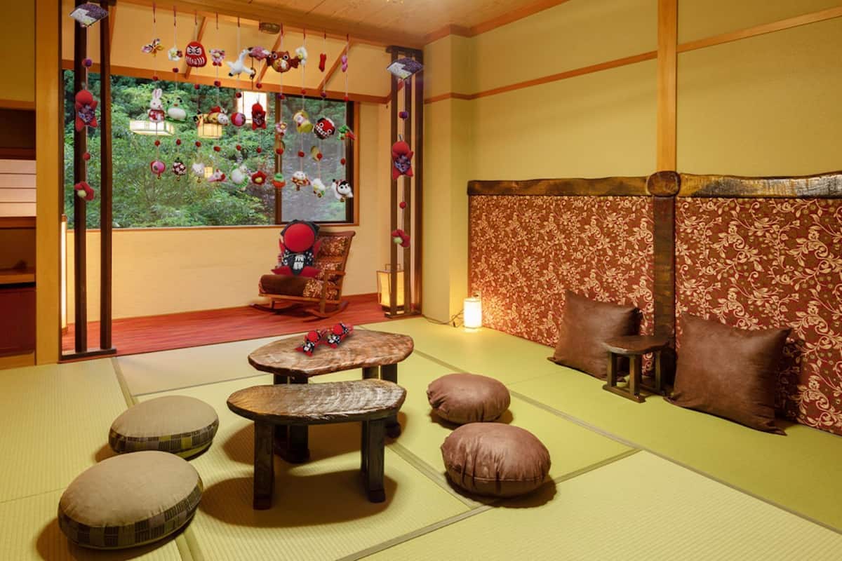 Um quarto japonês tradicional com piso de tatame, televisão, uma poltrona de balanço e uma parede decorativa com enfeites pendurados.