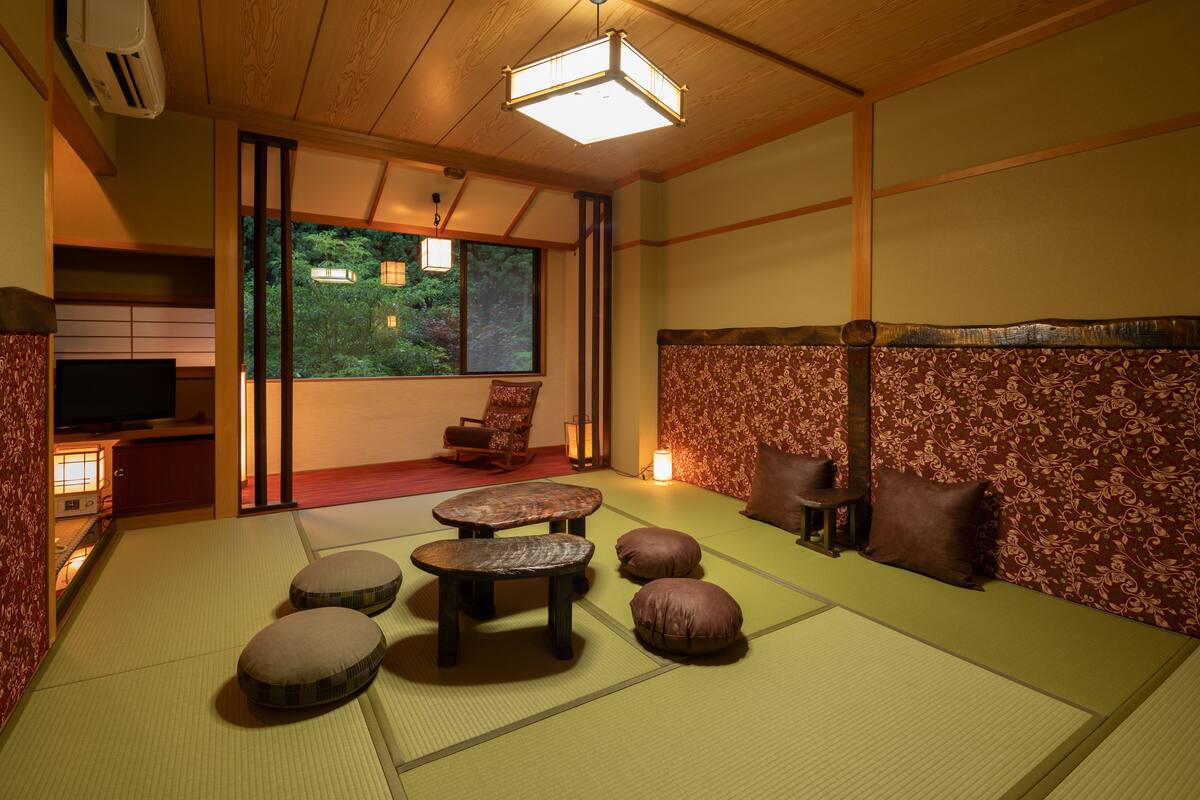 Um quarto japonês tradicional com tatames, uma mesa baixa, almofadas e uma televisão.