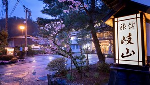 Un edificio japonés tradicional con un letrero, rodeado de cerezos en flor y una calle mojada al anochecer.