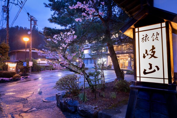 A traditional Japanese building with a signboard, surrounded by cherry blossoms and a wet street at dusk. - Ryokan Gizan (Takayama)