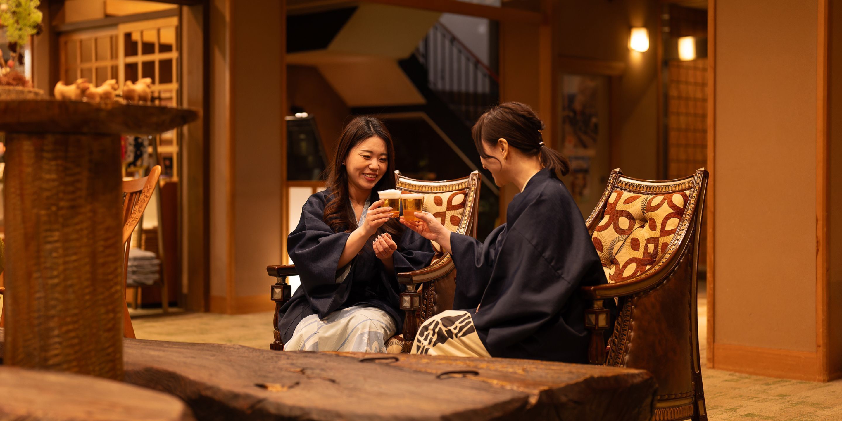 Two people sitting on ornate chairs in a warmly lit room with traditional decor.