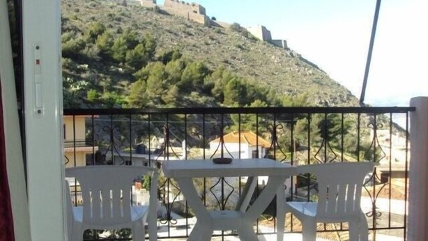 A balcony with two white chairs and a table, overlooking a hill with ruins. - Hotel Vasilis (Nafplio)