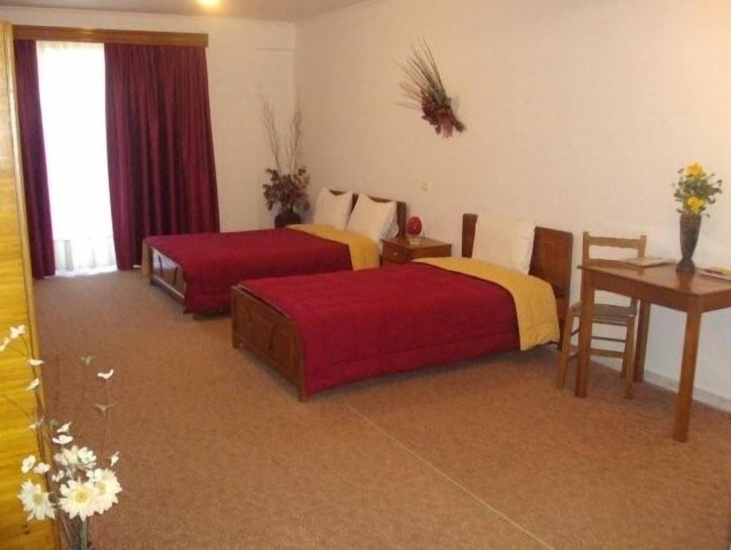 A hotel room with two single beds, a wooden nightstand, a small table, and a chair.