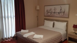 A hotel room with a bed, a nightstand, a lamp, and a painting of horses on the wall. - Hotel Vasilis (Nafplio)