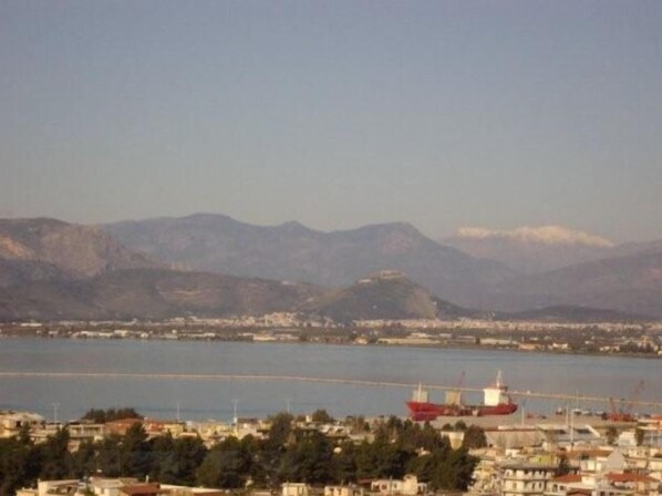 A coastal cityscape with a large red cargo ship docked at a port, surrounded by residential buildings and mountains in the background. - Hotel Vasilis (Nafplio)