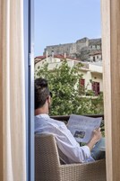 Un hombre lee un periódico en una silla de mimbre con vista a un edificio y árboles.