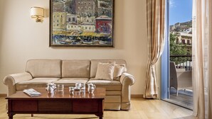 A living room with a beige sofa, a coffee table, a painting, and a view through a window. - Xenon Inn (Nafplio)